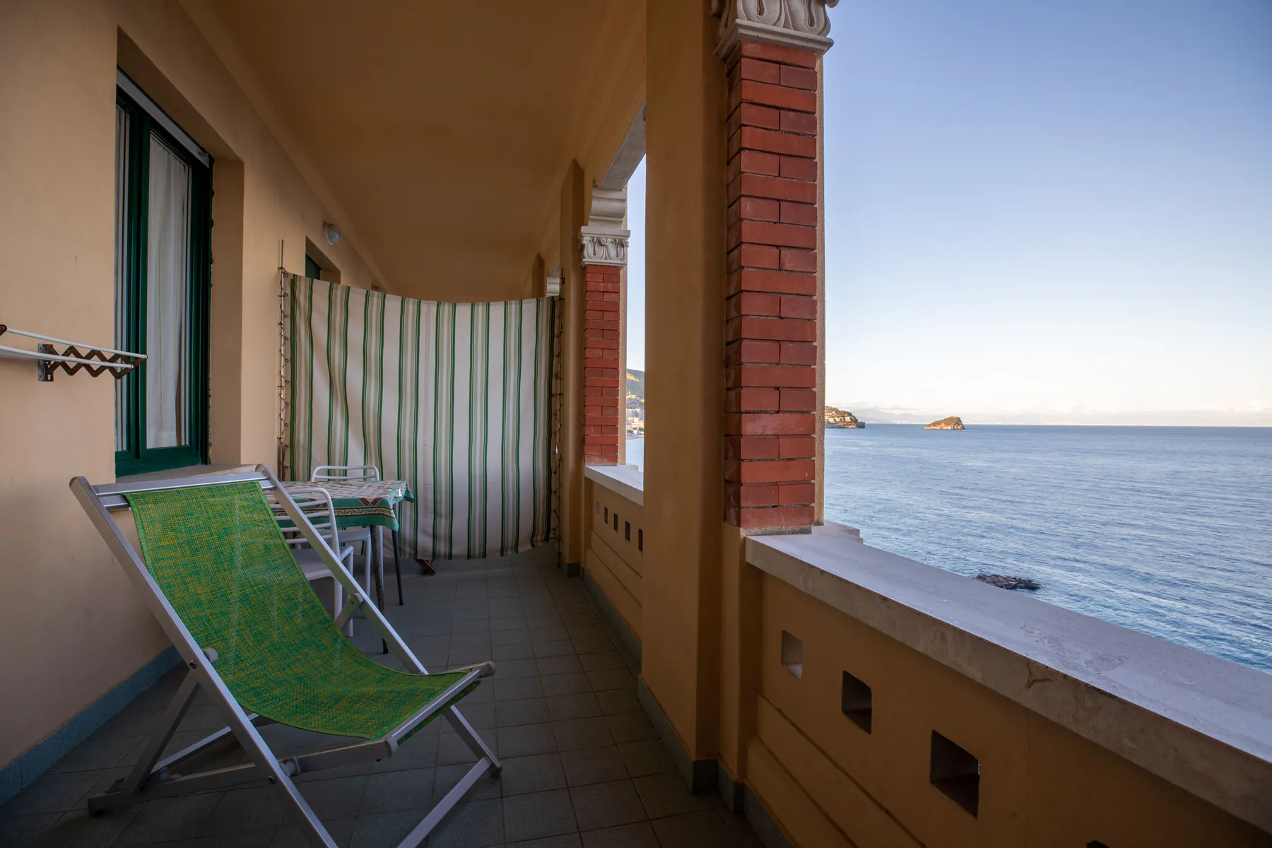 A room’s balcony with a deck chair, a small table and a view of the sea