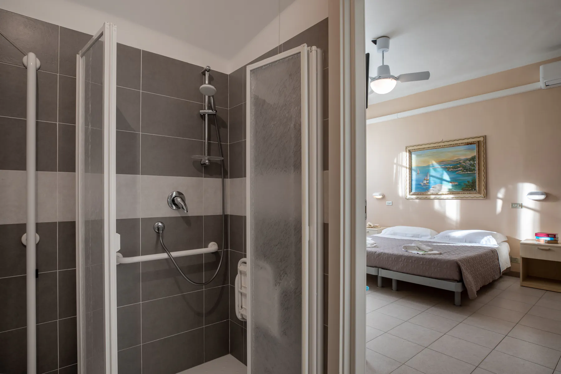 Bathroom with a walk-in shower and grab bars, next to a double room with a double bed