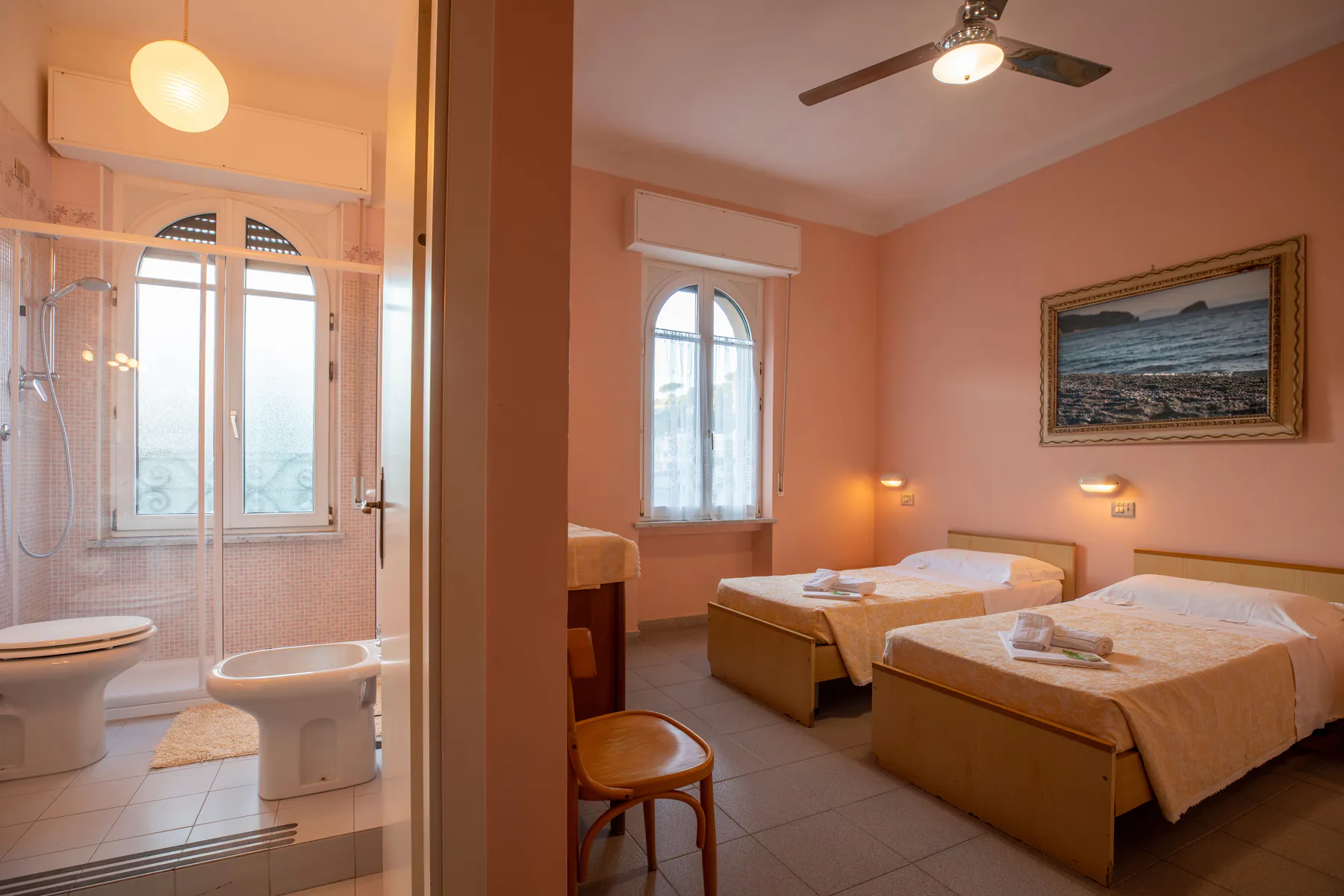 Room with two single beds, a seascape painting on the wall and a bathroom with shower