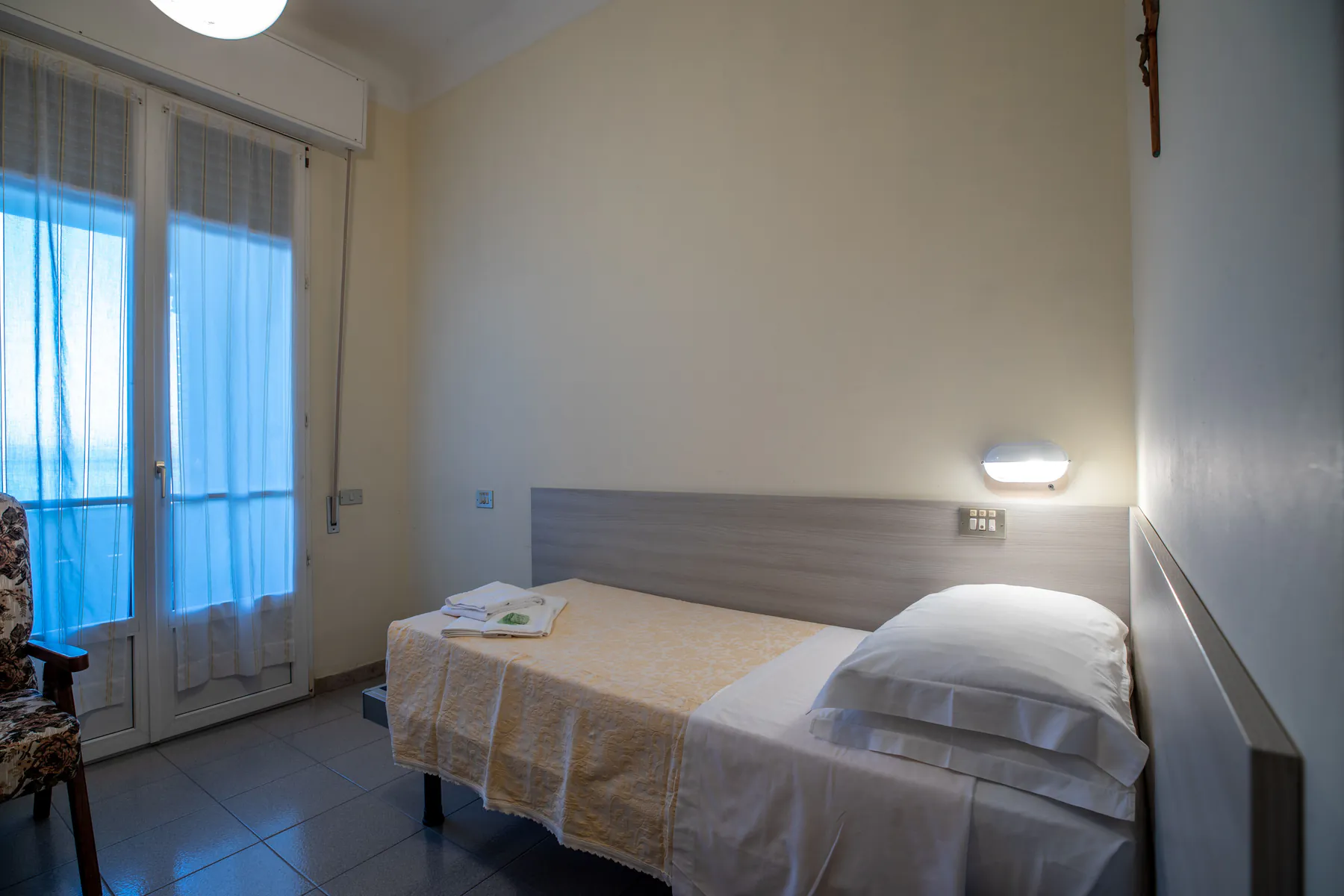 Bright single room with a bed, a bedside table and a French window