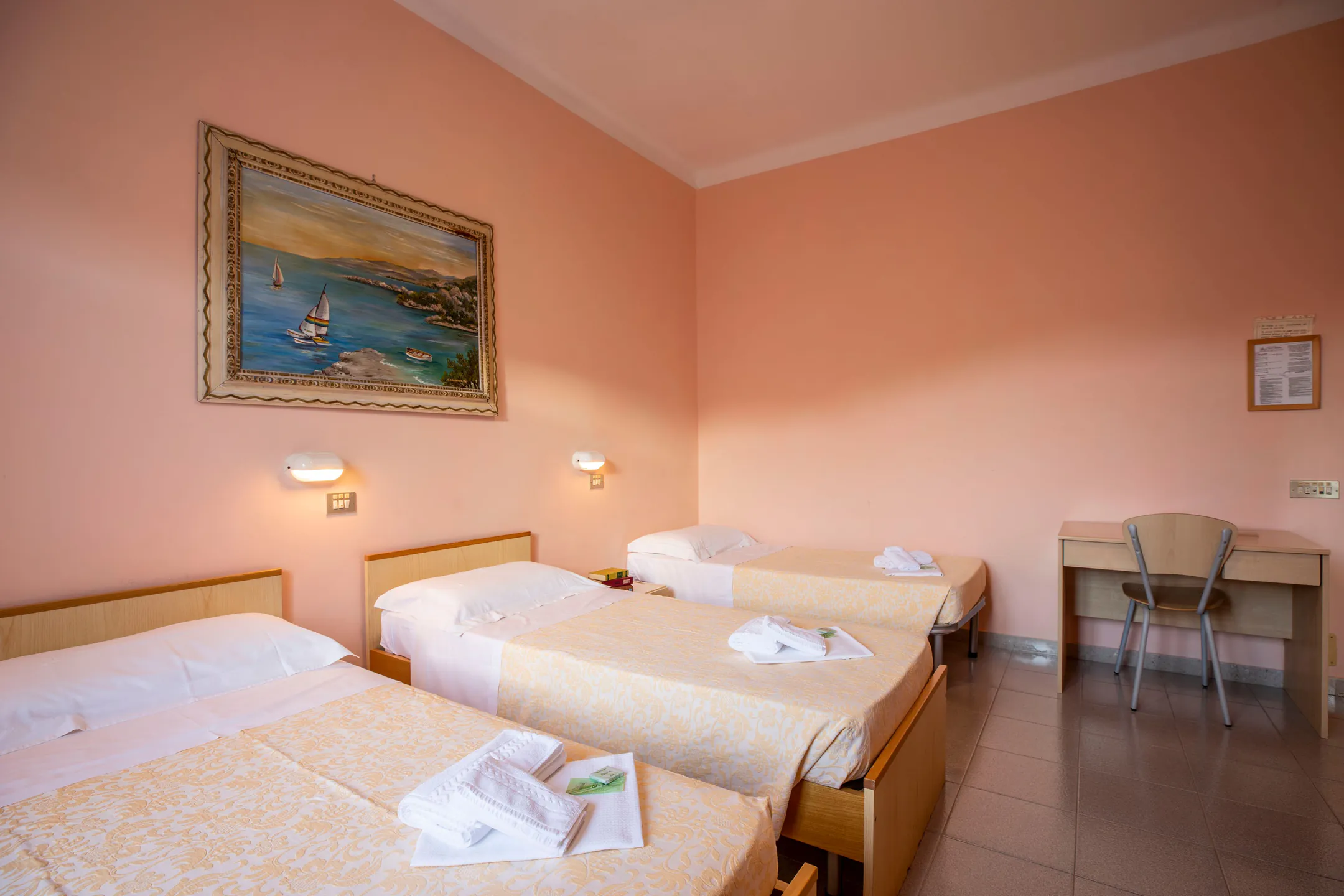 Triple room with pink walls, three beds and a painting of a bay