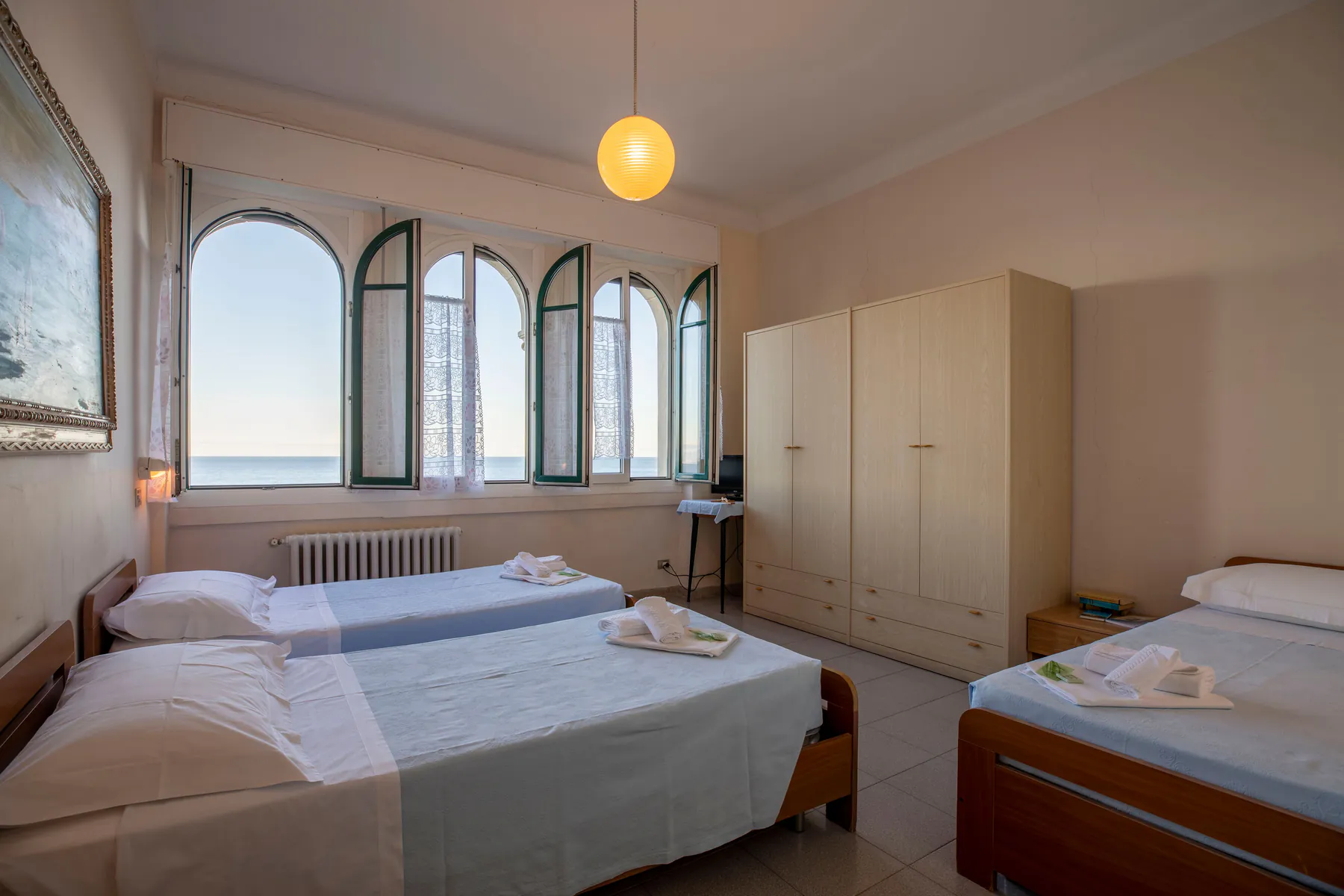 Triple room with three beds, a wardrobe and arched windows overlooking the sea