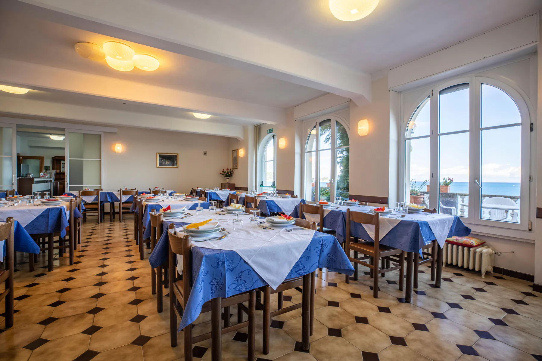 La sala da pranzo con tavoli apparecchiati e grandi finestre ad arco sul mare