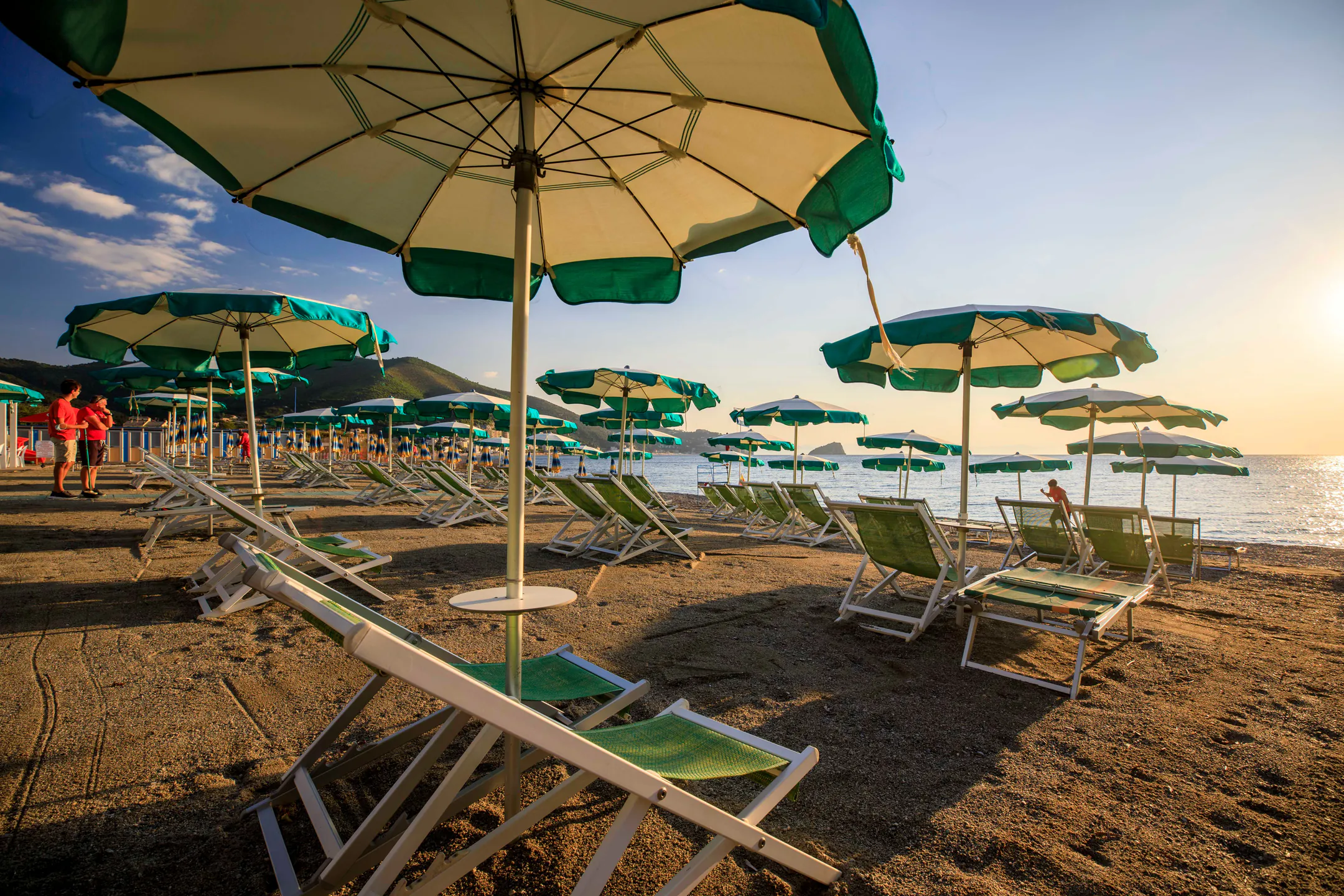 Ombrelloni verdi e sdraio sulla spiaggia privata di primo mattino, con il mare sullo sfondo
